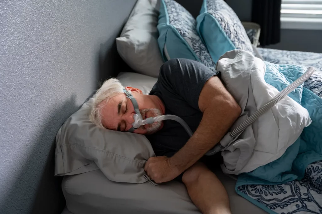 An old man sleeps with a CPAP machine in bed to treat his sleep apnea