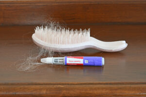 Semaglutide pen next to a hair brush with hair in it to show how semaglutide mght cause hair loss.